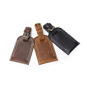 Handcrafted full grain leather luggage tag in brown, featuring white stitching and an adjustable strap with a brass buckle for secure attachment to luggage